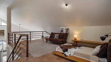 A spacious loft bedroom with a large bed, a brown leather sofa, a wooden bench, a small table, and a staircase.