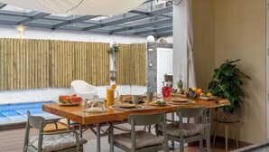 Comedor con piscina al fondo, una mesa de madera y sillas.