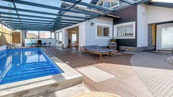 A covered outdoor swimming pool with adjacent lounge chairs and a patio area.