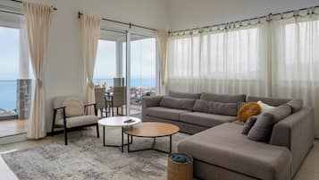 A modern living room with a grey sofa, a round coffee table, and a view of the sea through large windows.