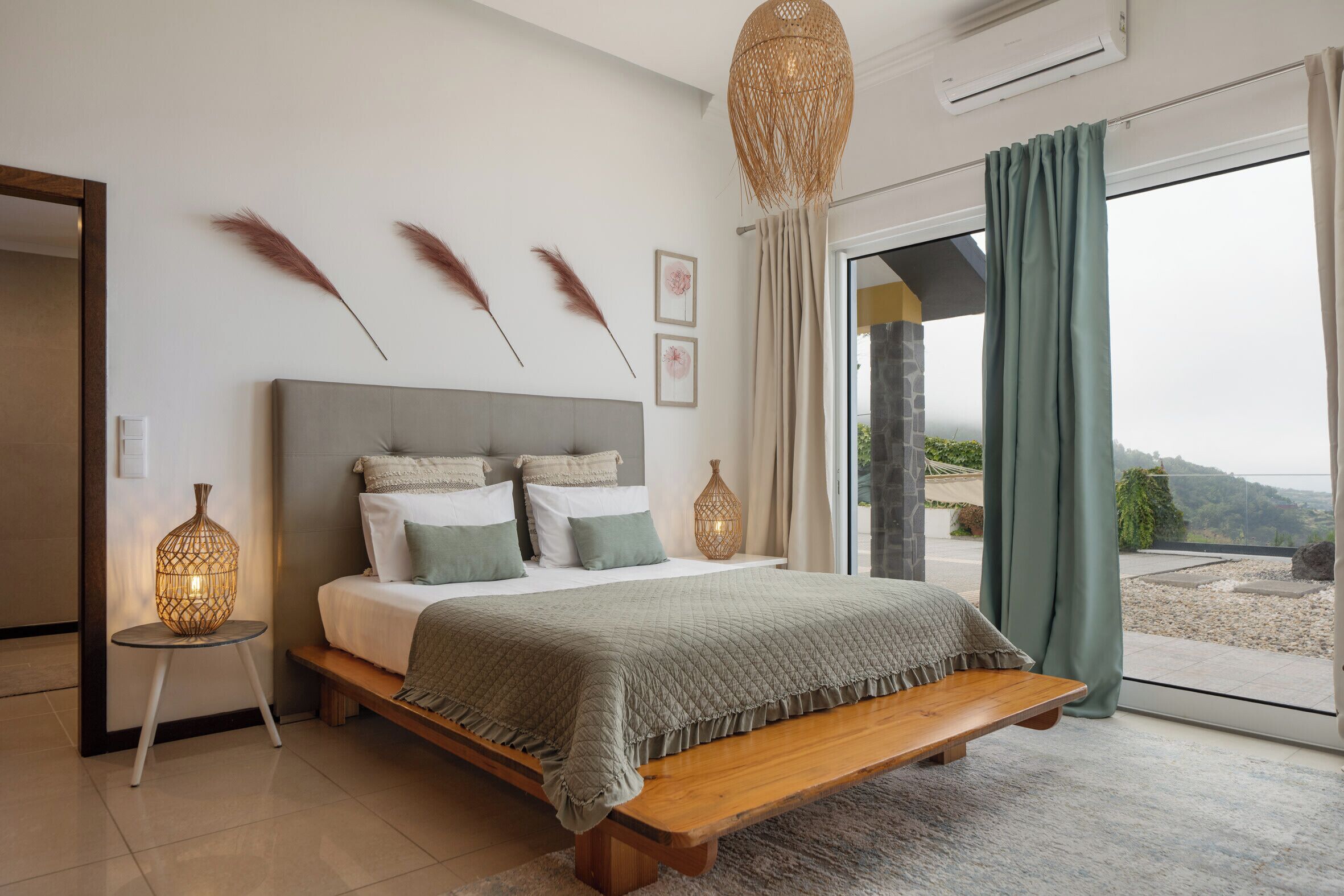 A bedroom with a large bed, bedside lamps, a bench, and a view through a glass door.
