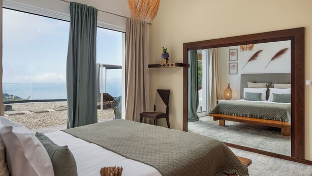 Un dormitorio con una cama grande, una silla, un espejo y vistas al mar.