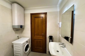 Une petite salle de bain équipée d’un lave-linge, d’un évier, d’un miroir et d’une porte.