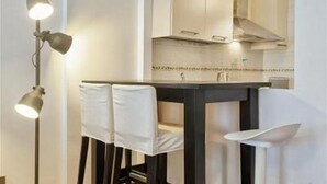 A modern kitchen with a dark countertop, white chairs, and pendant lighting.