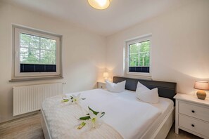 Une chambre à coucher comprenant un lit, deux tables de chevet, une commode, une fenêtre et un radiateur.