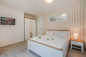 A bedroom with a bed, bedside table, nightstand, mirror, and a painting on the wall.