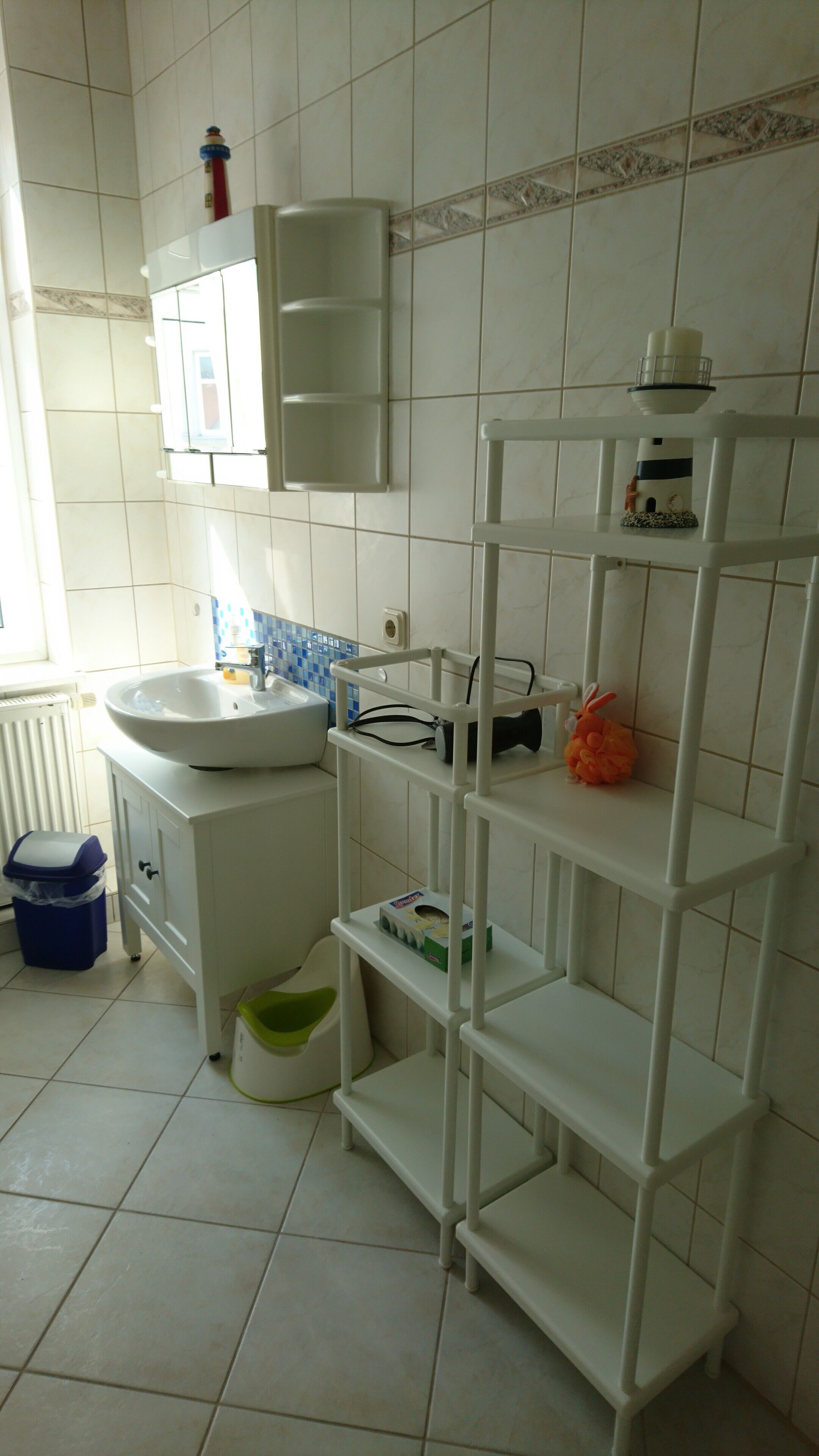 A bathroom with a white sink, a mirror, a shelf with toiletries, and a small window.
