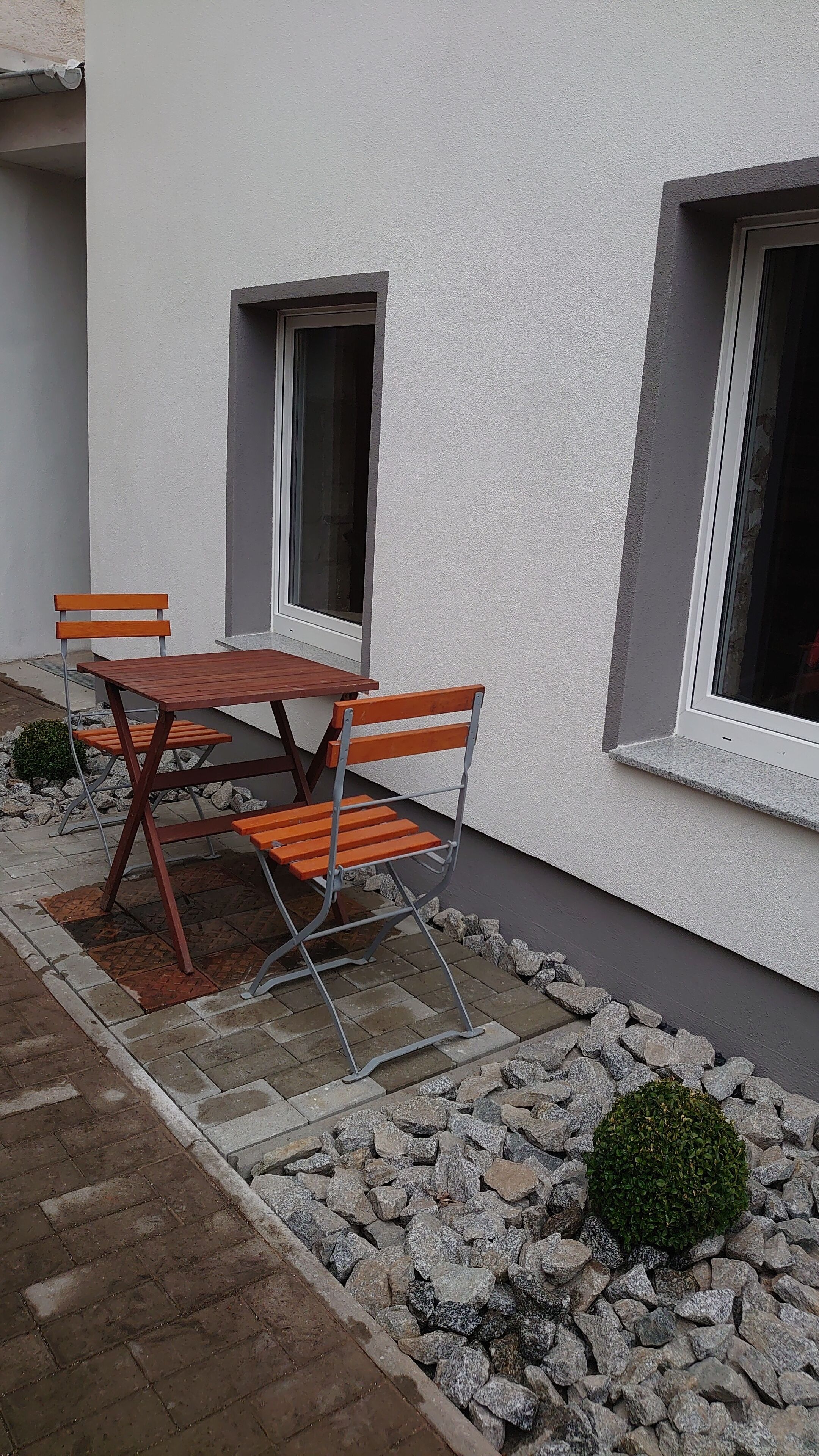 Un espacio al aire libre con mesa y sillas, una ventana pequeña y un jardín de rocas.