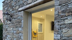 A stone exterior with a glass door leading to an interior with wooden flooring and a visible window. - Very nice air-conditioned apartment with heated pool in charming villa. (Oletta)