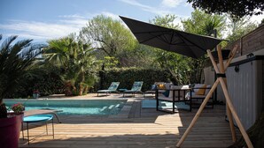 A wooden deck with a pool, lounge chairs, and a table. - Very nice air-conditioned apartment with heated pool in charming villa. (Oletta)