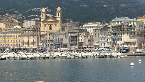 A coastal town with a prominent church, marina with boats, and residential buildings. - Very nice air-conditioned apartment with heated pool in charming villa. (Oletta)