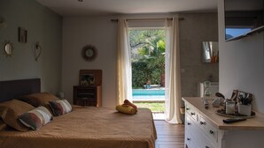 A bedroom with a large bed, a dresser, and a view of a swimming pool. - Very nice air-conditioned apartment with heated pool in charming villa. (Oletta)