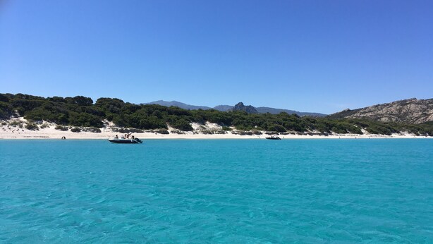A boat on a clear turquoise sea with a beach and rocky hills in the background. - Very nice air-conditioned apartment with heated pool in charming villa. (Oletta)