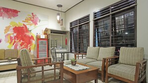Un salon comprenant un canapé, des fauteuils, une table basse et une grande fenêtre équipée de stores.