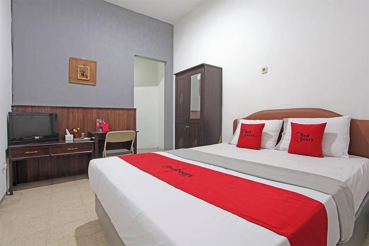 Een hotelkamer met een bed, een bureau met een televisie, een kledingkast en een lijst aan de muur.