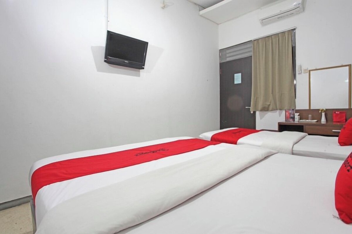 Une chambre d’hôtel avec deux lits, un téléviseur fixé au mur, un bureau avec un miroir et une fenêtre avec des rideaux.