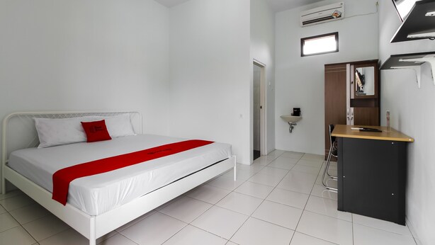 A modern bedroom with a white bed, a red accent, a small desk, and a built-in wardrobe. - RedDoorz @ Jagakarsa 2 (Jakarta)