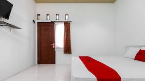 A hotel room with a bed, a TV mounted on the wall, a door, and a window with curtains. - RedDoorz @ Jagakarsa 2 (Jakarta)