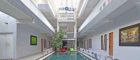 An indoor swimming pool with a central staircase, white walls, and a ceiling with hanging lights.