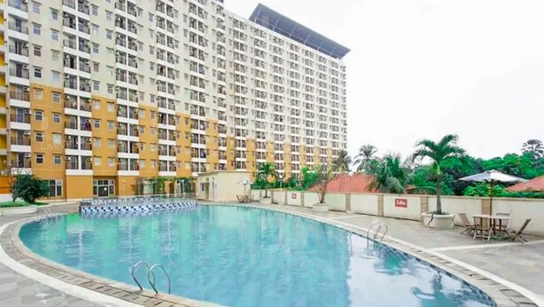 A swimming pool with a tiled deck, surrounded by a high-rise building with multiple balconies. - RedLiving Apartemen Margonda Residence - Tower 2 (Depok)
