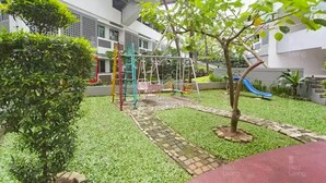 A courtyard with a playground, including swings and a slide, surrounded by greenery and a paved walkway. - RedLiving Apartemen Margonda Residence - Tower 2 (Depok)