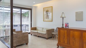 A room with a wicker sofa, a wooden cabinet, and a glass door leading to an outdoor area. - RedDoorz @ Malabar Street (Bandung)