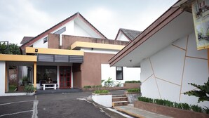 A modern building with a yellow and white facade, a red door, and a small outdoor seating area. - RedDoorz near Alun-alun Kota Sukabumi (Sukabumi)
