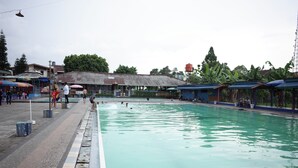 A swimming pool with people around it, a covered area with benches, and a building in the background. - RedDoorz near Alun-alun Kota Sukabumi (Sukabumi)