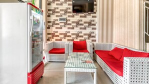 A room with a white sofa set, a glass coffee table, a TV mounted on the wall, and a refrigerator.