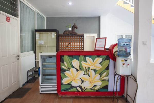 A reception area with a water dispenser, a decorative horse sculpture, a glass display case, and a door with a number sign. - RedDoorz near Museum Angkut Batu 2 (Batu)