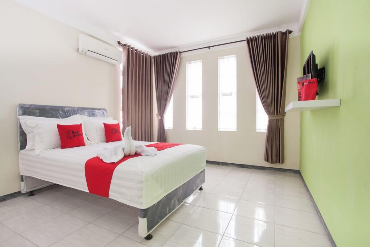 A hotel room with a bed, curtains, a shelf with items, and a window.