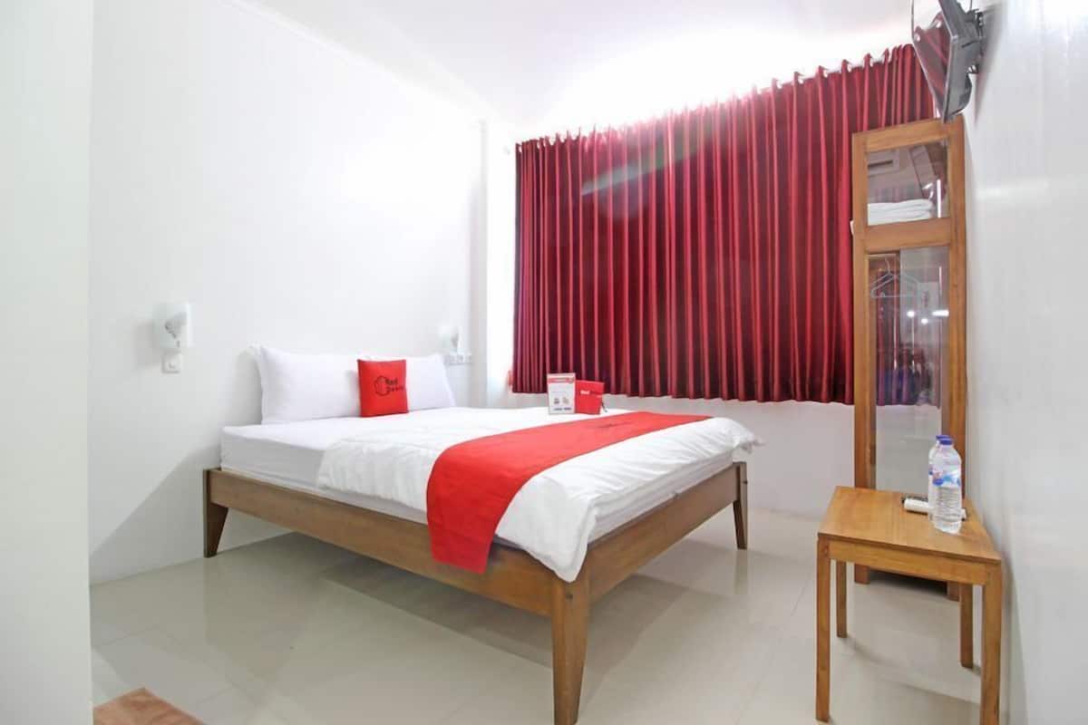 Una habitación de hotel con cama, una mesita, un espejo y ventana con cortinas rojas.