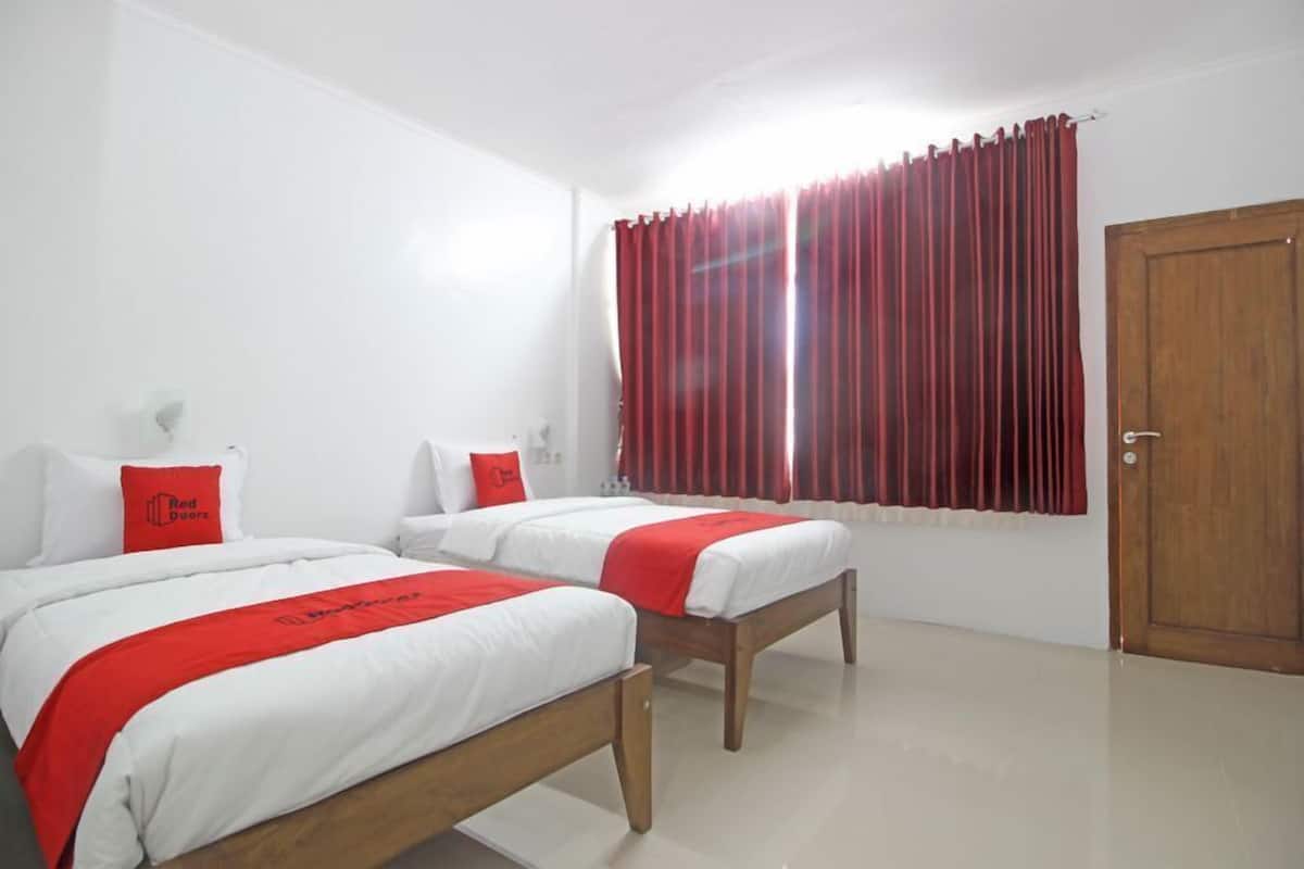 Habitación de hotel con dos camas, detalles en rojo, una puerta de madera y una ventana con cortinas rojas.