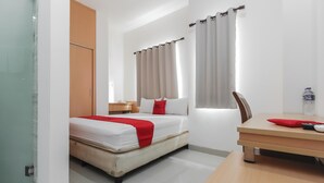 Une chambre d’hôtel avec un lit, une table en bois, une chaise, une fenêtre avec des rideaux et une petite table sur laquelle se trouve une bouteille.