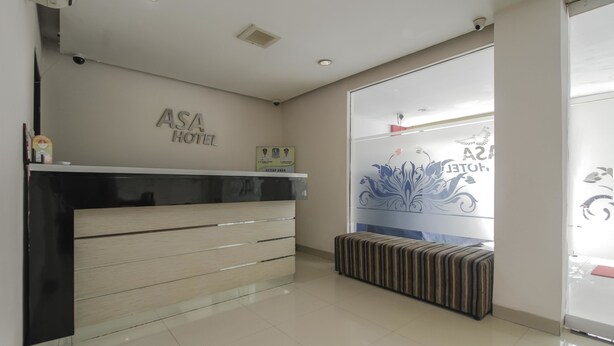Un espace d’accueil d’hôtel au design moderne, comprenant un comptoir d’accueil, un banc et un mur portant le nom de l’hôtel.