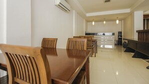 Un coin repas avec une table et des chaises en bois, une cuisine à l’arrière-plan et un appareil de climatisation fixé au mur.