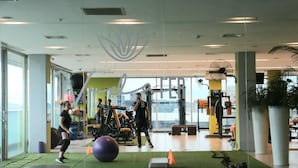 Un gimnasio con equipo de ejercicio, un ventilador grande y una pelota de ejercicio verde.
