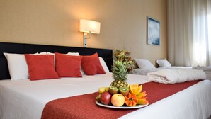 Una habitación de hotel con una cama bien hecha, un plato de frutas sobre la cama, una lámpara y un cuadro en la pared.