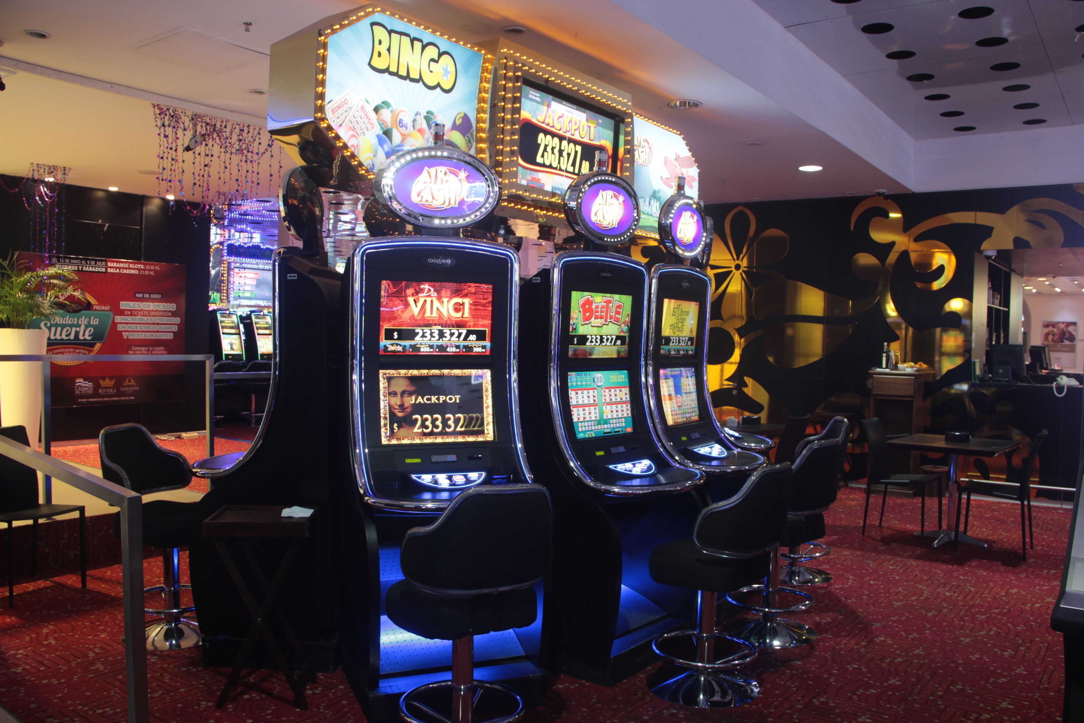 A casino with slot machines, bar stools, and a red carpeted floor.