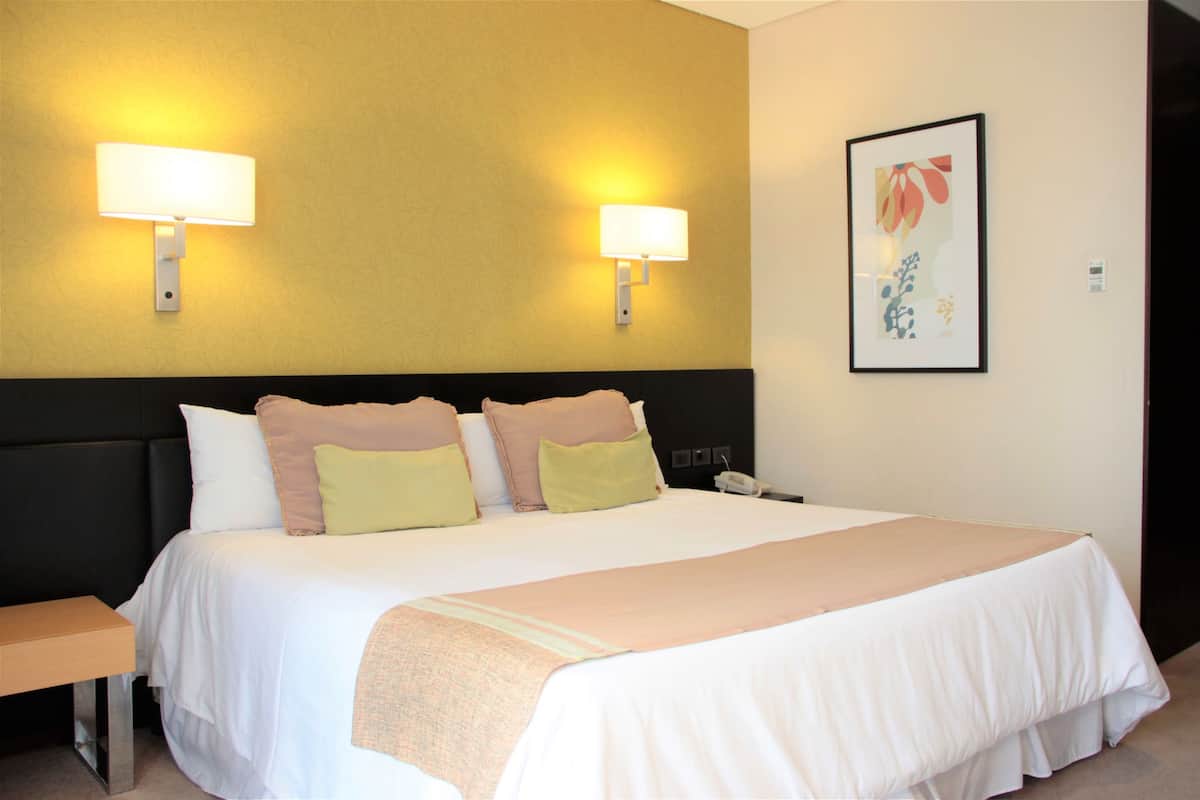 A hotel room with a large bed, two bedside lamps, a bedside table, and a framed artwork on the wall.