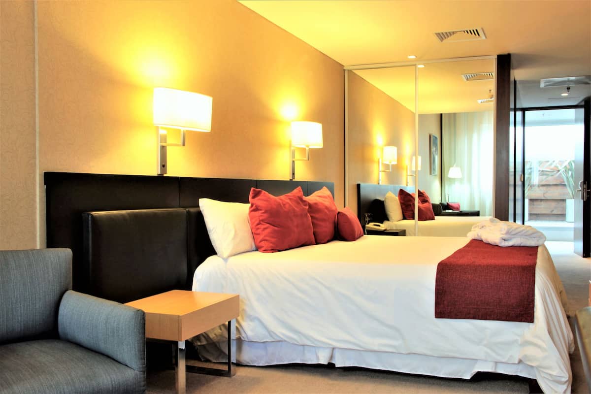 A hotel room with a bed, a sofa, a small table, and a mirror.