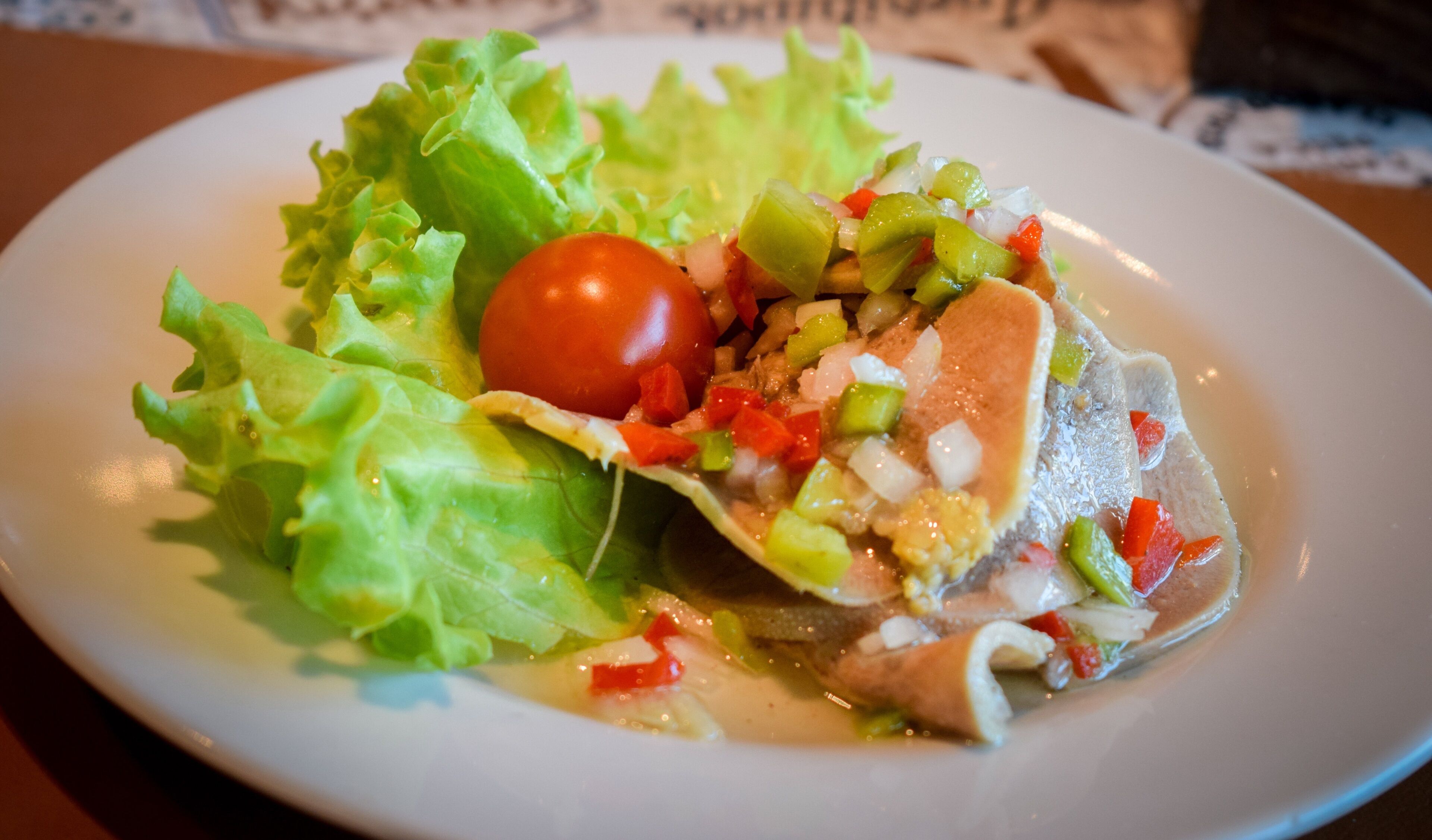 A plate with a fish fillet, lettuce, and a cherry tomato.