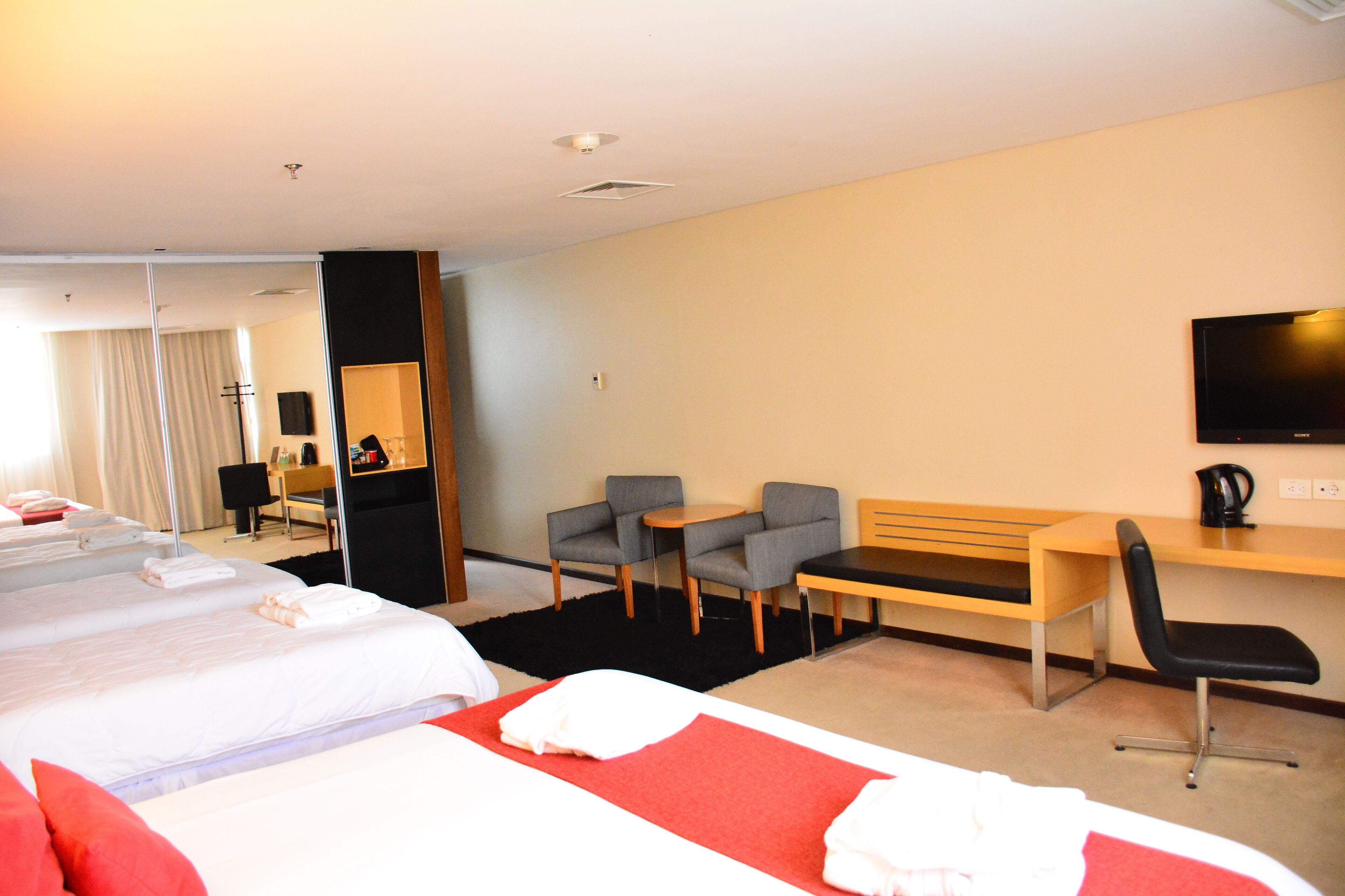Een hotelkamer met twee bedden, een bureau, een stoel, een televisie en een spiegel.
