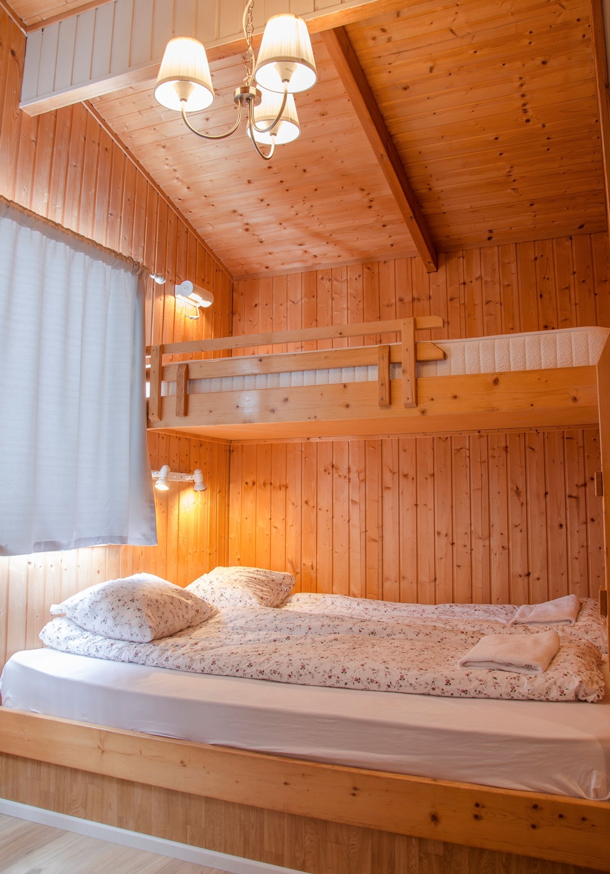 Une pièce de cabane en bois avec un lit superposé, une fenêtre avec des rideaux et un luminaire au plafond.