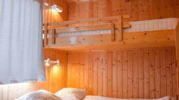 Une pièce de cabane en bois avec un lit superposé, une fenêtre avec des rideaux et un luminaire au plafond.
