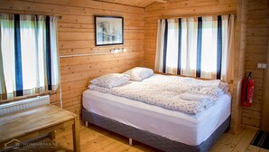 Habitació d'una cabana de fusta amb un llit, una taula petita i un quadre al mur.