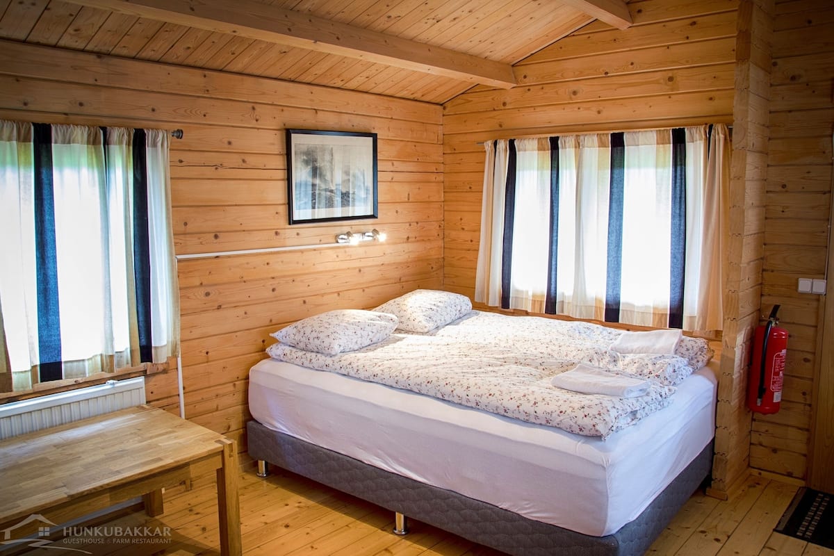 Une pièce de cabane en bois comprenant un lit, une petite table et un tableau encadré accroché au mur.
