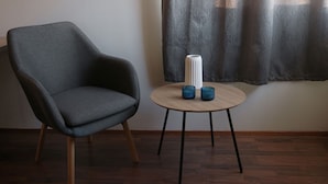 Habitació moderna amb una poltrona gris, una taula rodona petita amb dos suportantues de vela blaus i un vas blanc.