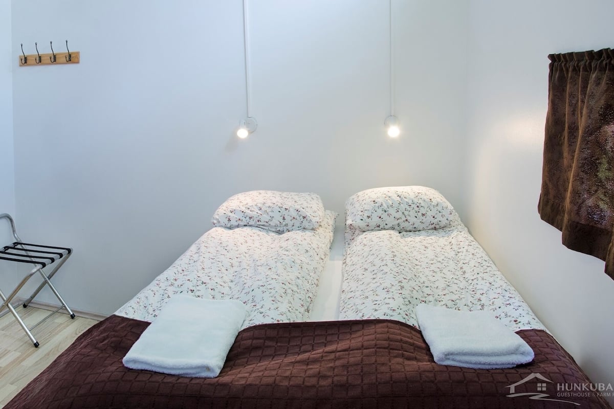 Une petite pièce propre, avec deux lits, un étendoir et une porte en bois.