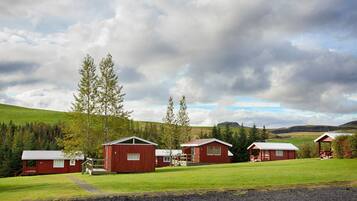 A row of red cabins with a grassy field and trees in the background.